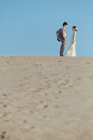 青空の下浜岡砂丘で向き合い立つ夫婦のウェディングフォト