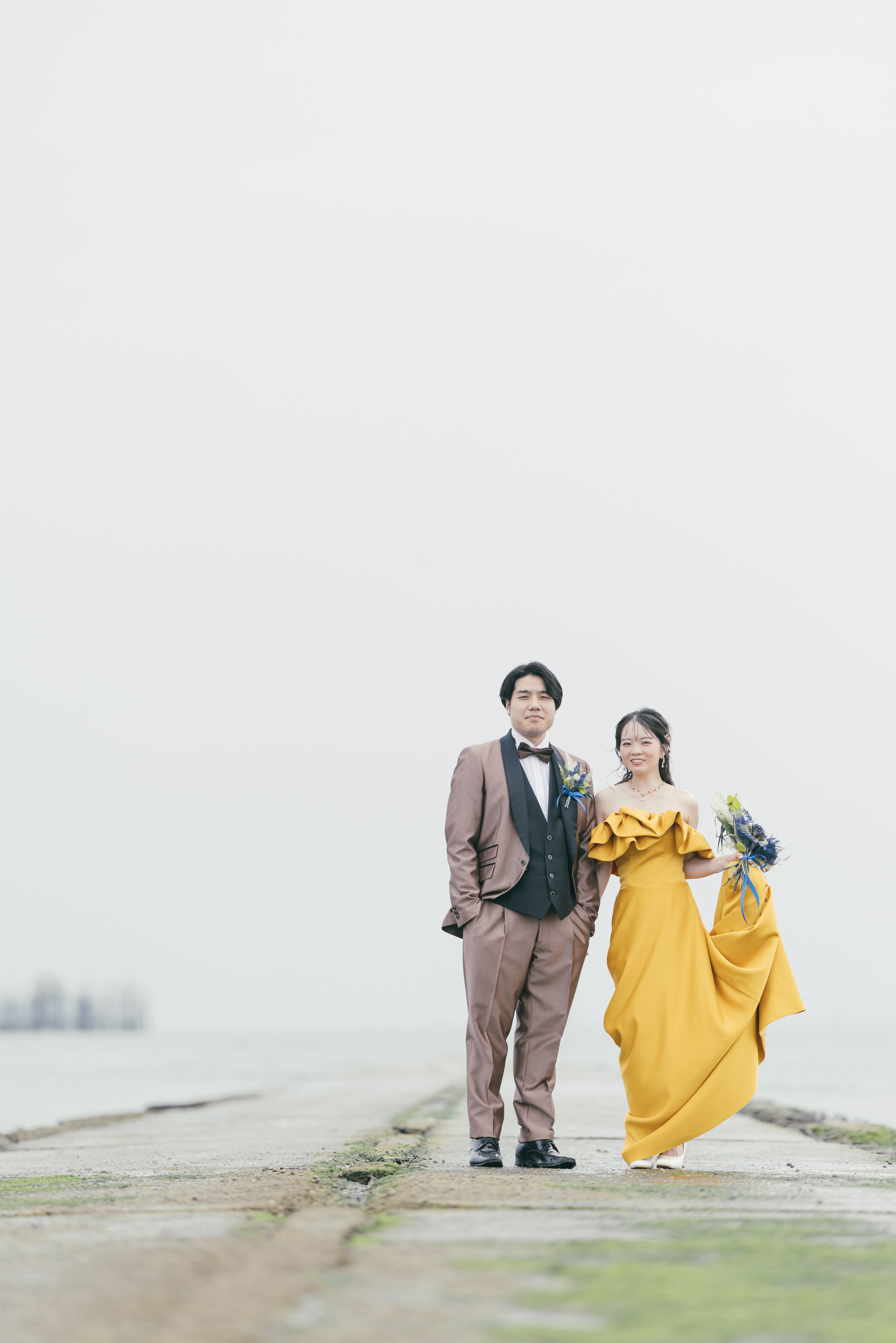 海岸で笑顔で並ぶ夫婦のウェディングフォト