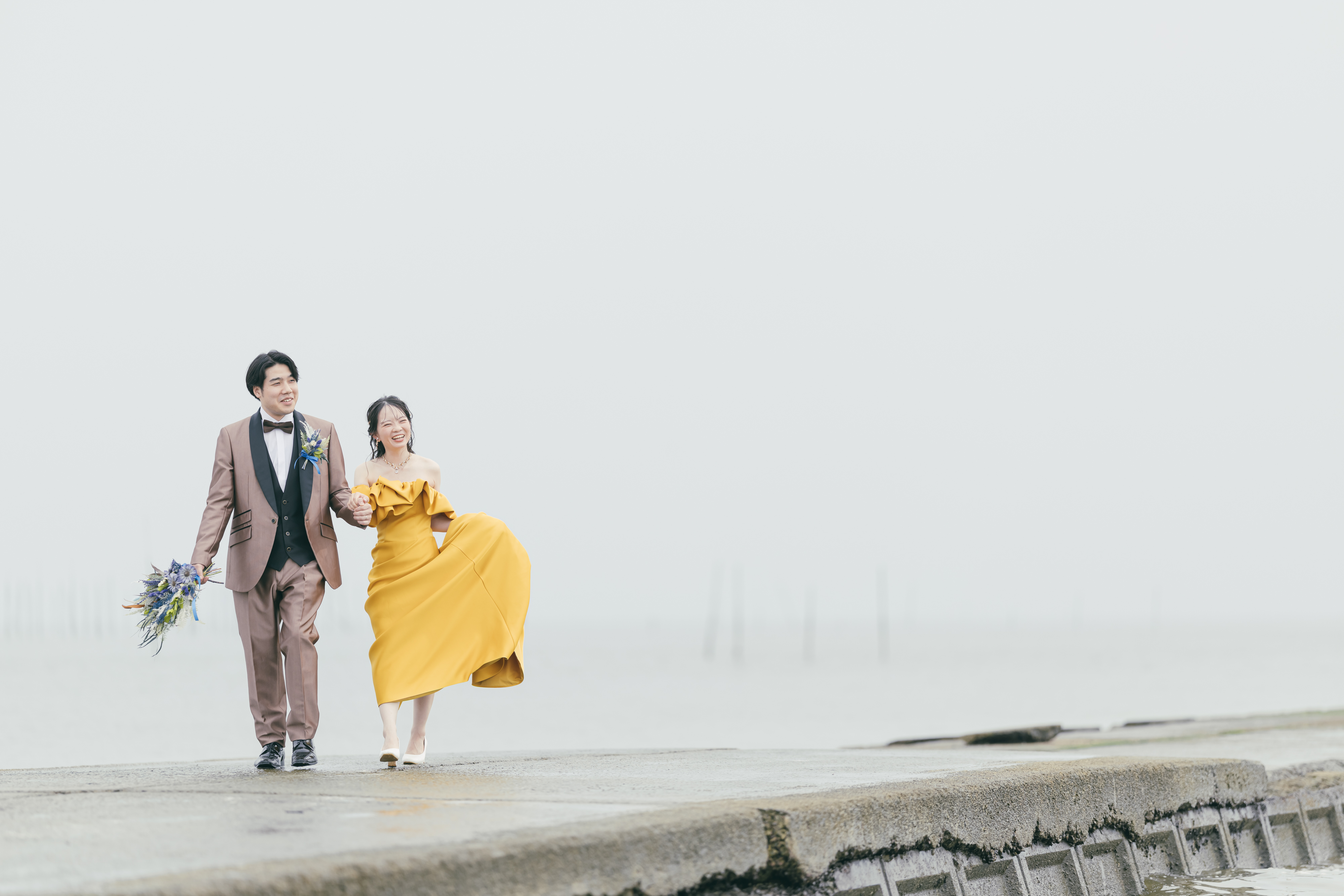 海岸で笑顔で並び歩く夫婦のウェディングフォト