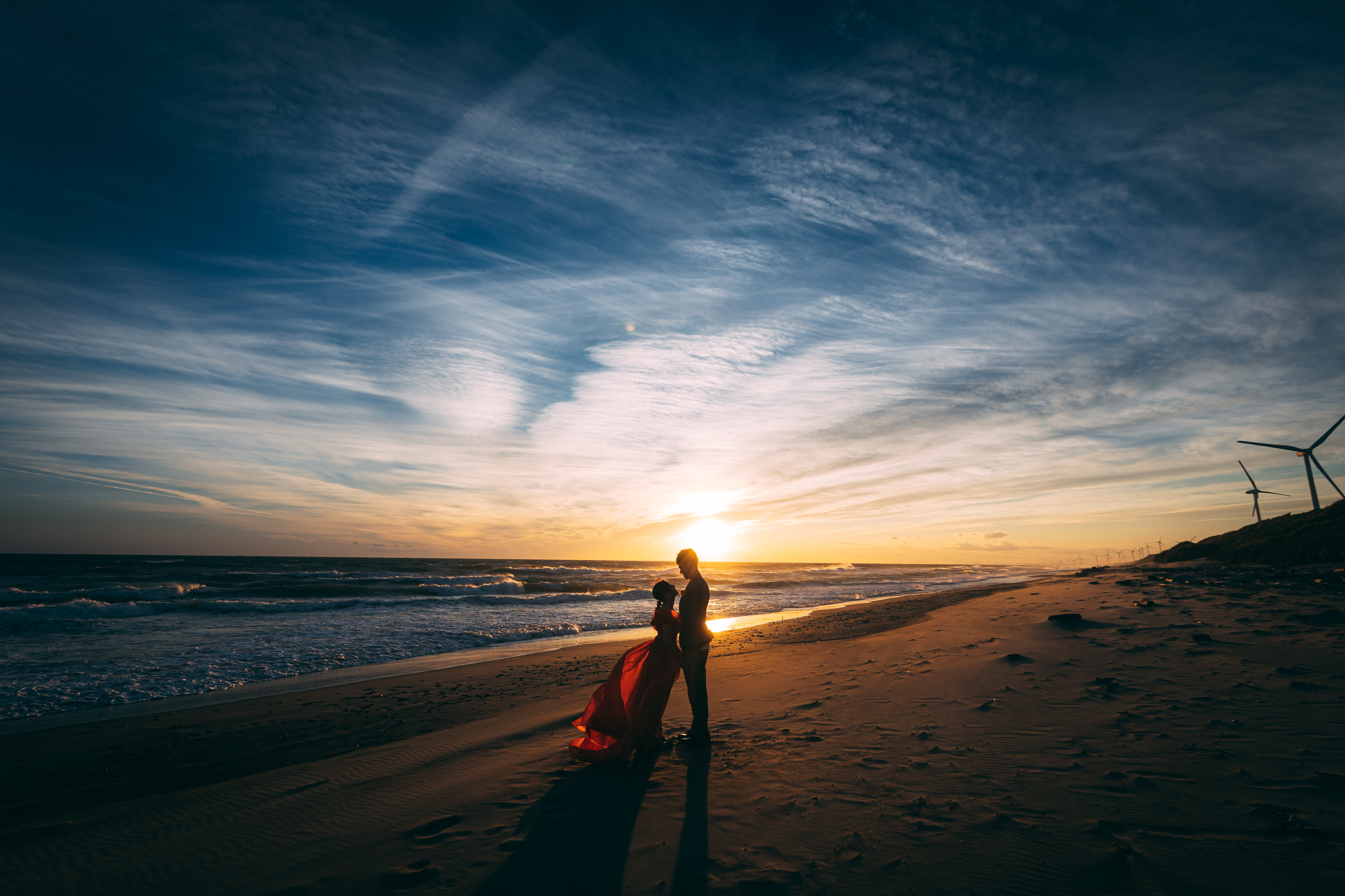 浜辺で夕日をバックに向き合う夫婦のウェディングフォト