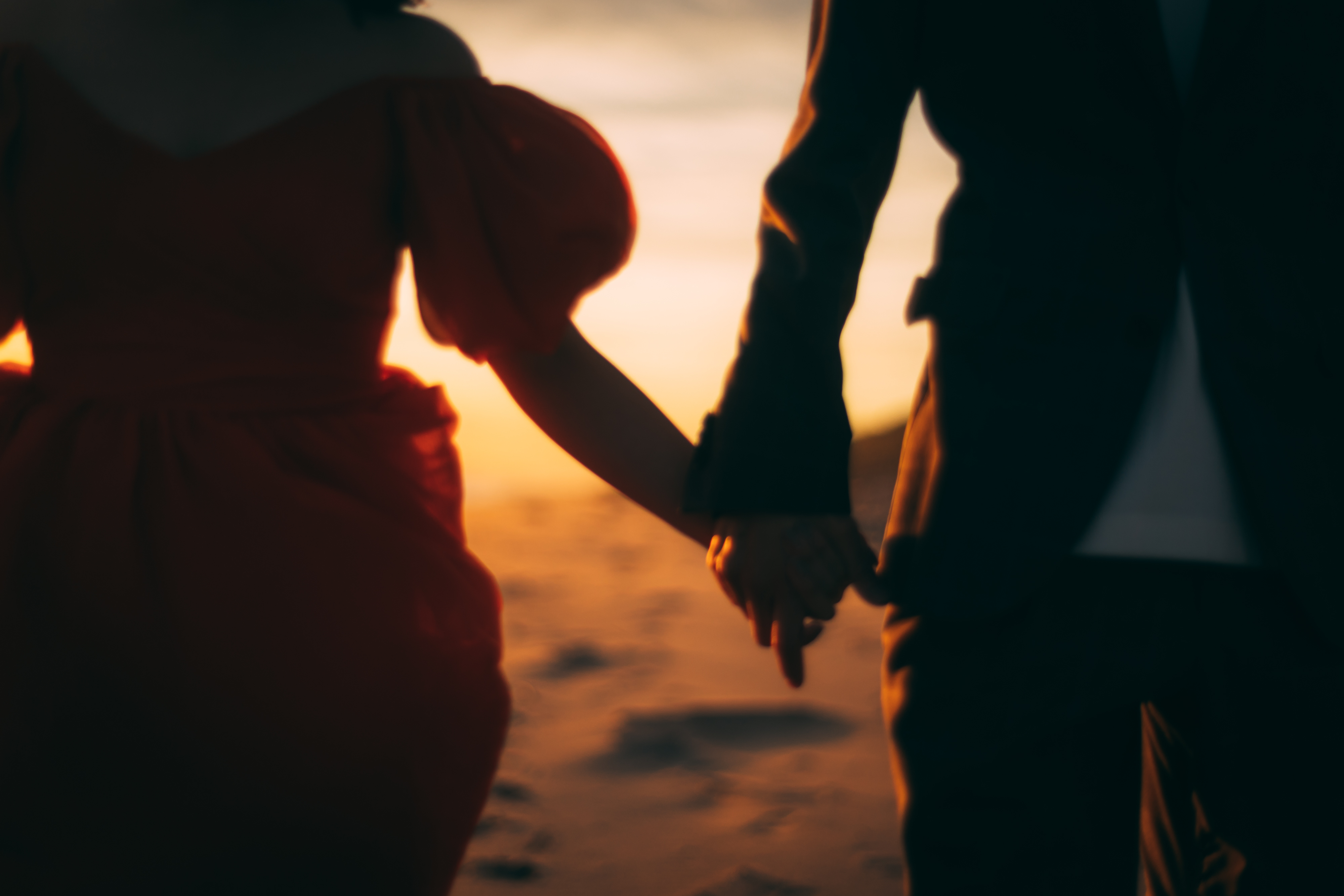 浜辺で夕日をバックに手を繋ぐウェディングフォト