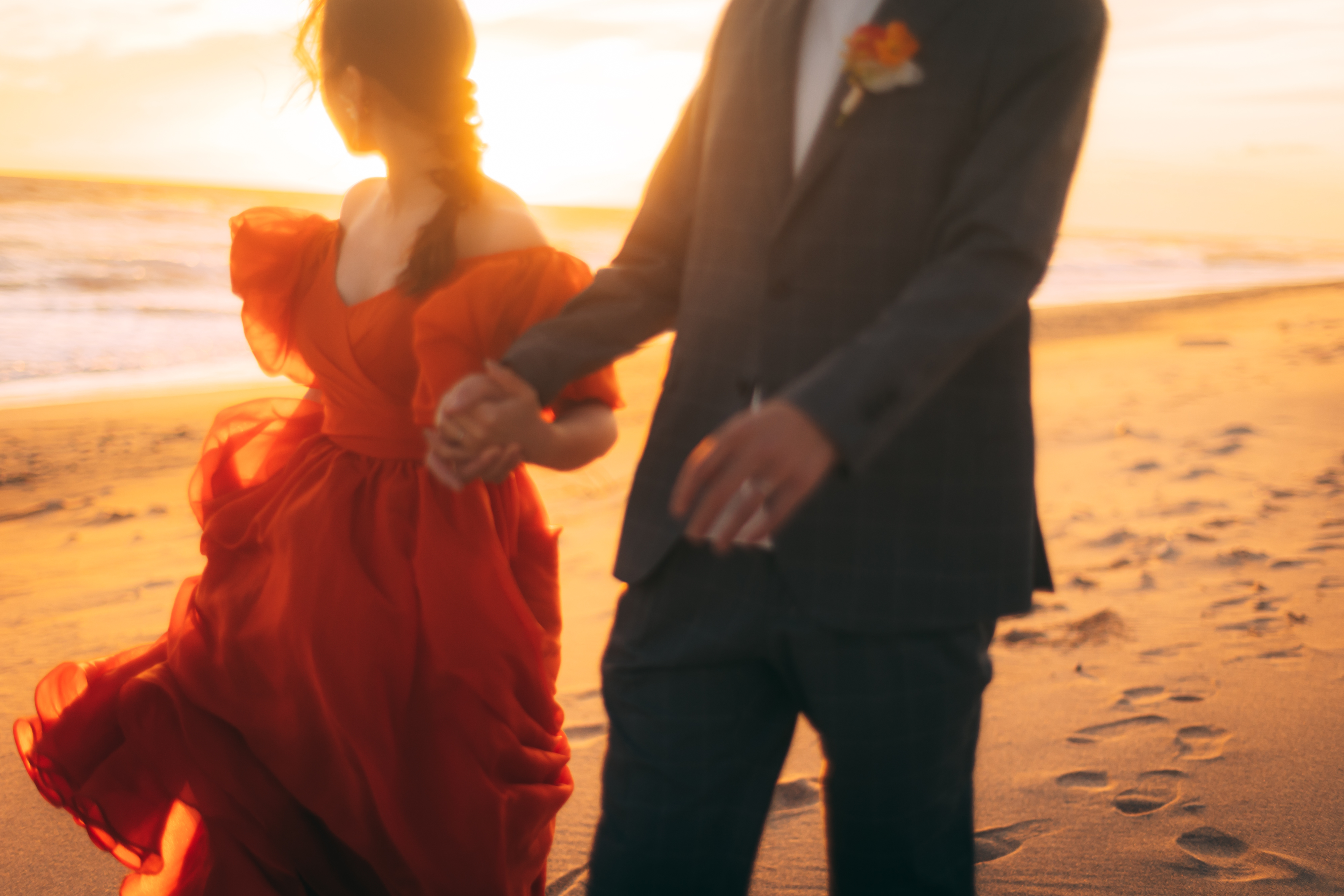 浜辺で夕日をバックに手を繋ぐ夫婦のウェディングフォト