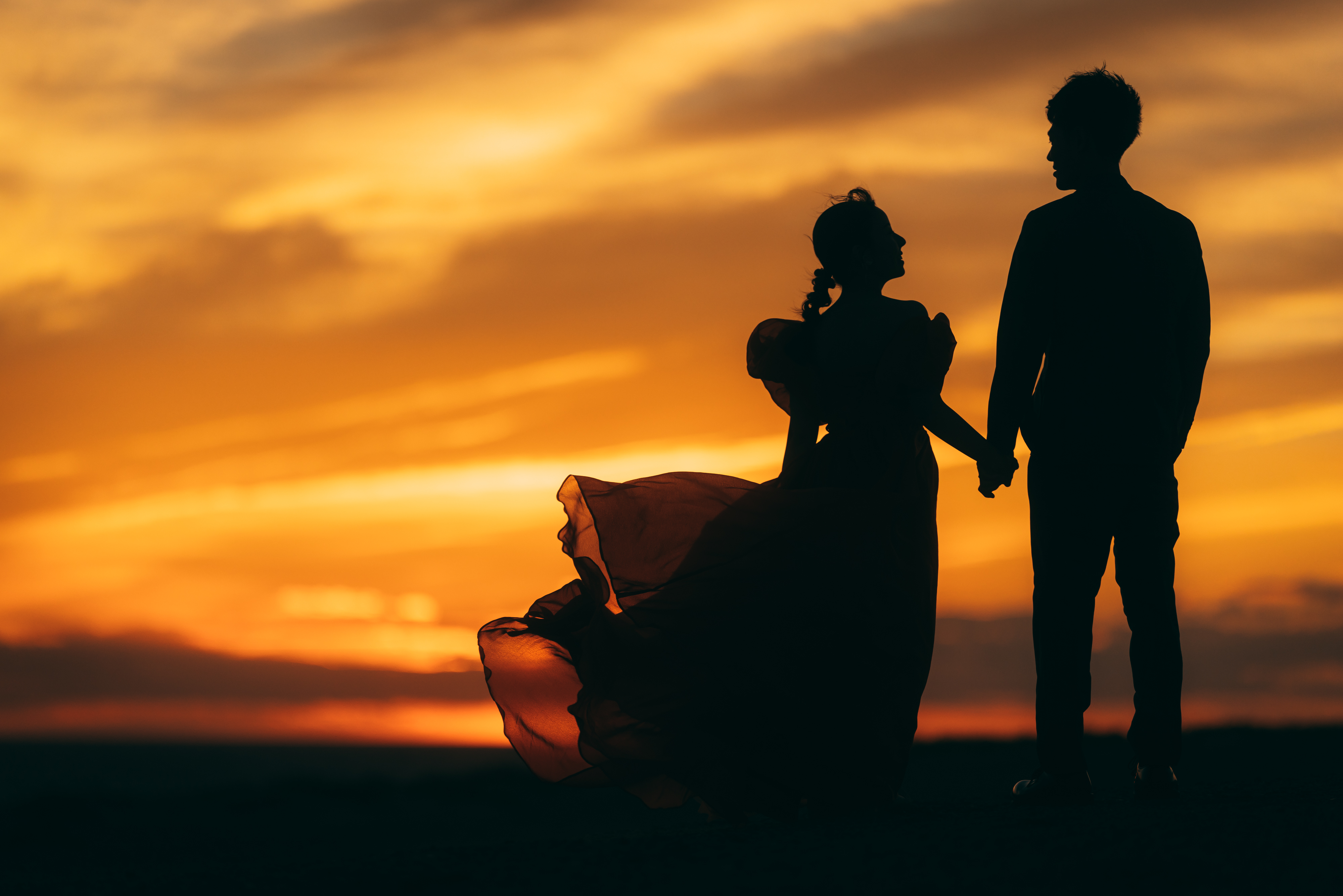 浜辺で夕日をバックに手を繋ぎ向き合う夫婦のウェディングフォト