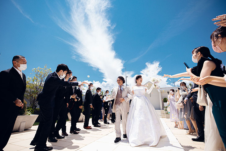 青空の下参列者に祝福される新郎新婦のウェディングフォト